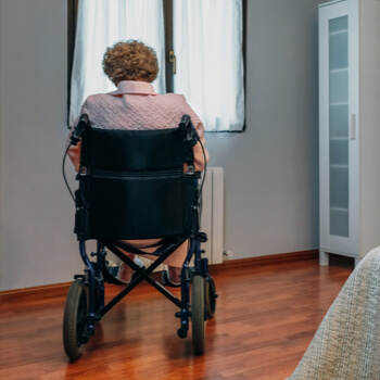 Elderly woman in wheelchair looking out the window of her room.