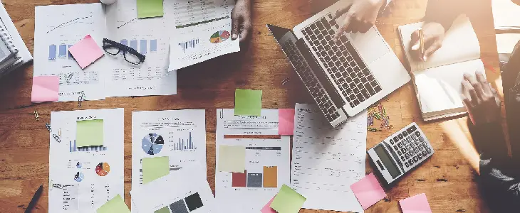 a table covered in papers with post it notes a laptop and calculator business planning