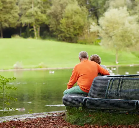Rear view of aged couple enjoying retirement, resting in park near pond